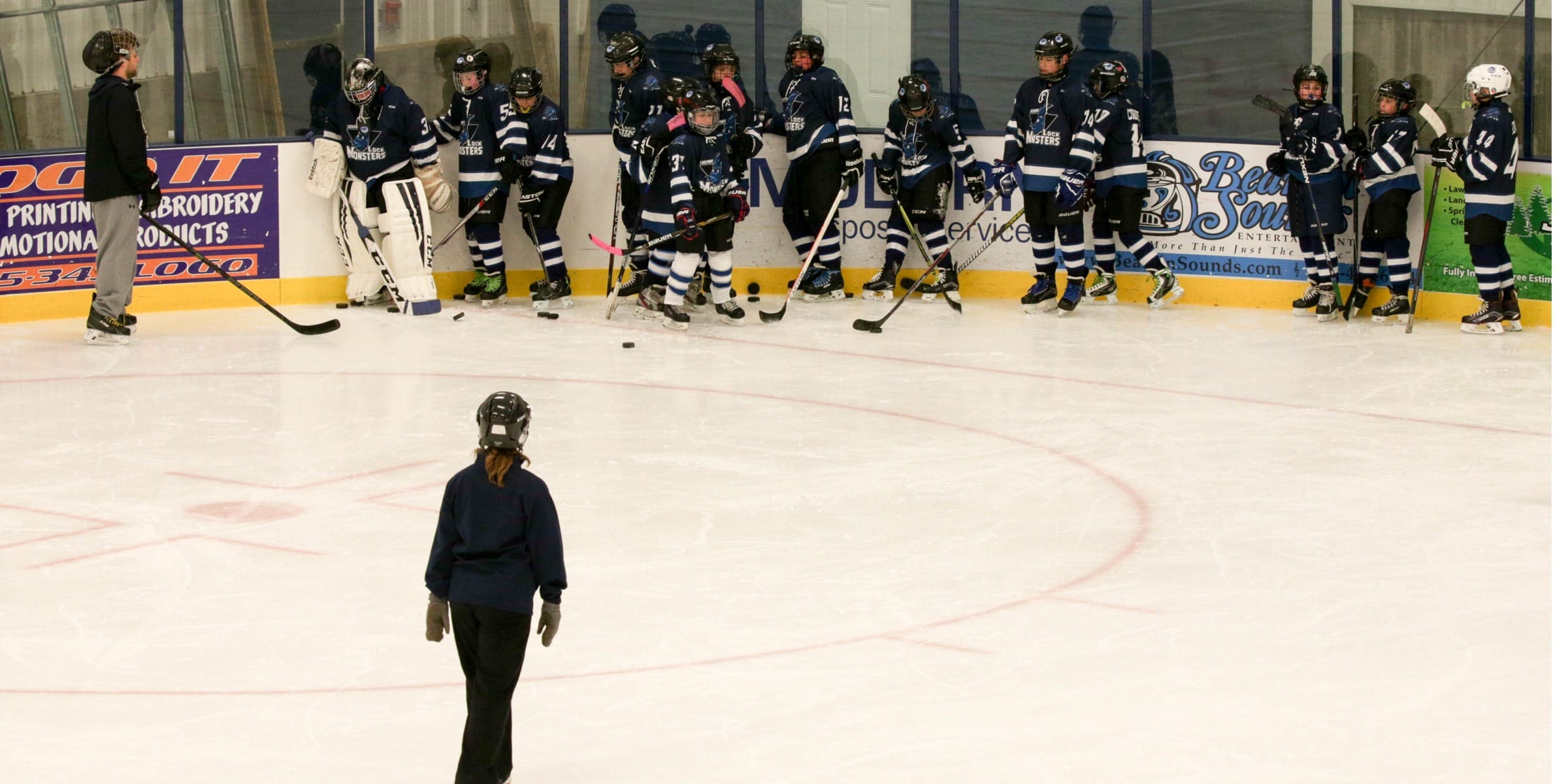hockey players lined up against the boards with a coach out on the ice